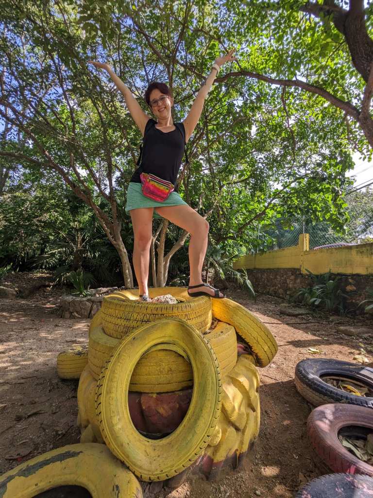 Ashley Schwartau standing triumphantly on a pile of tires painted yellow in Parque la Cieba, one of the best Kid-friendly activities in Playa del Carmen