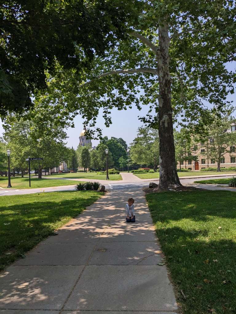 4 year old boy kneeling on sidewalk on Notre Dame campus