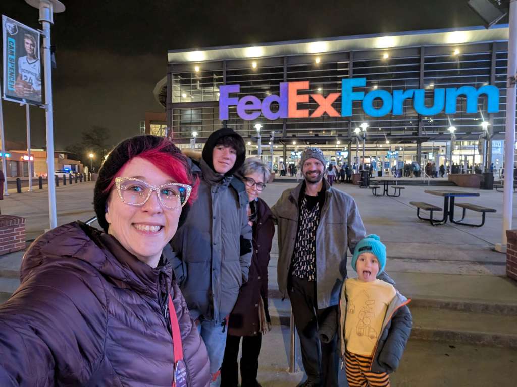 A family selfie outside the FedExForum, home of the Memphis Grizzlies, illuminated at night with colorful signage.