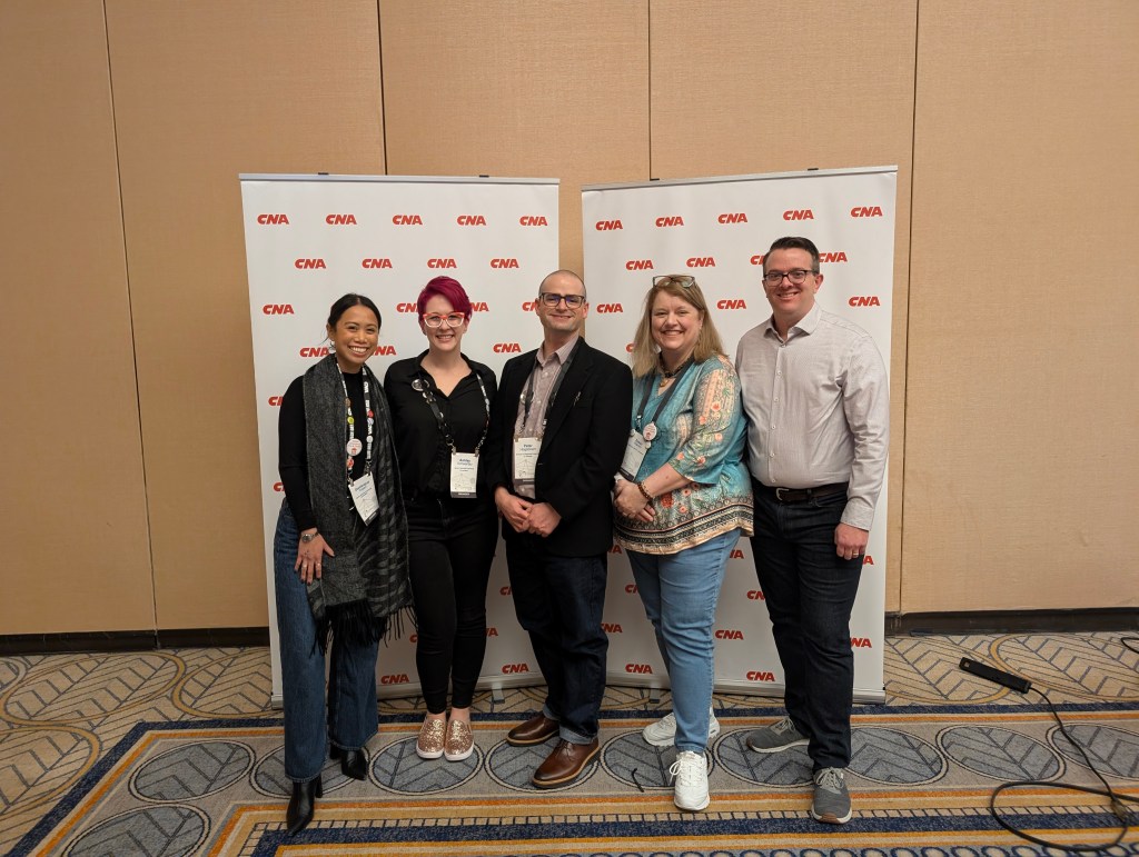 A group of five people posing together in front of a CWA branded backdrop, smiling and dressed in professional attire.